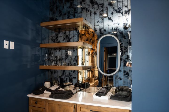 Wet bar with antiqued mirror tile backsplash, floating wood shelves, navy walls and white quartz counter in Avon, IN