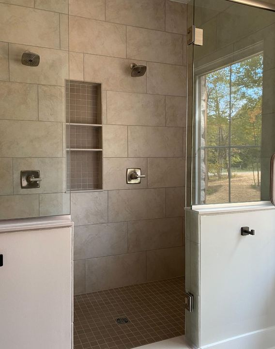 Walk-in shower with beige large-format tile, triple stacked niche, mosaic floor and frameless glass door in Avon, IN