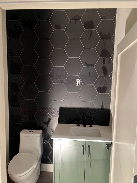 Powder room with oversized black hexagon tile accent wall behind a sage green vanity in Indianapolis, IN