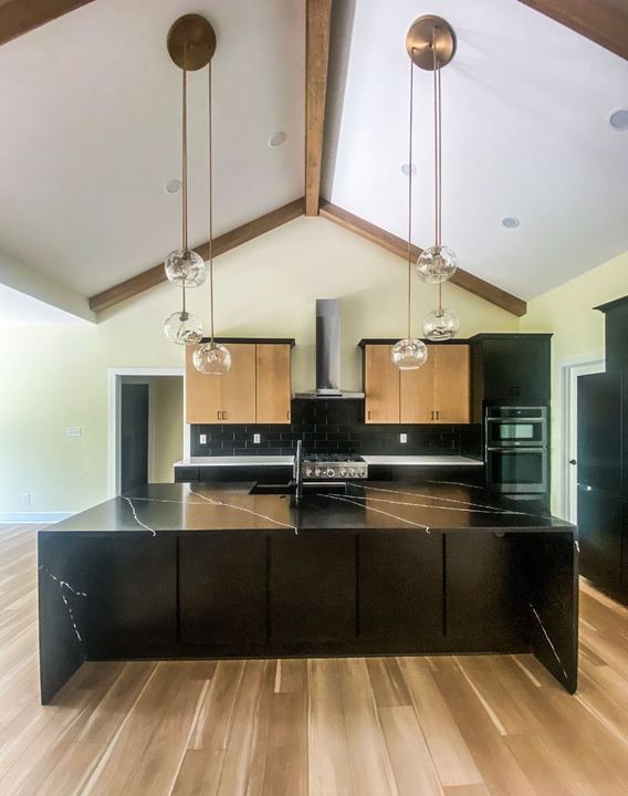 Vaulted kitchen with black subway tile backsplash, black quartz island and wood-look plank flooring in Avon, IN