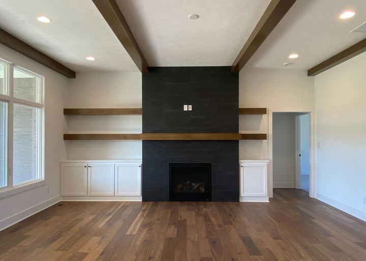 Floor-to-ceiling black tile fireplace wall with floating wood shelves and walnut hardwood floors in Avon, IN