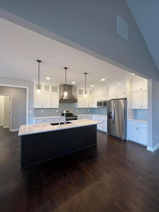 Kitchen with white cabinets, navy island, marbled quartz counters, blue glass tile backsplash and dark hardwood floor in Brownsburg, IN