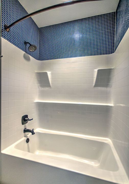 Tub and shower surround finished with navy blue square mosaic tile above and bronze fixtures in Avon, IN
