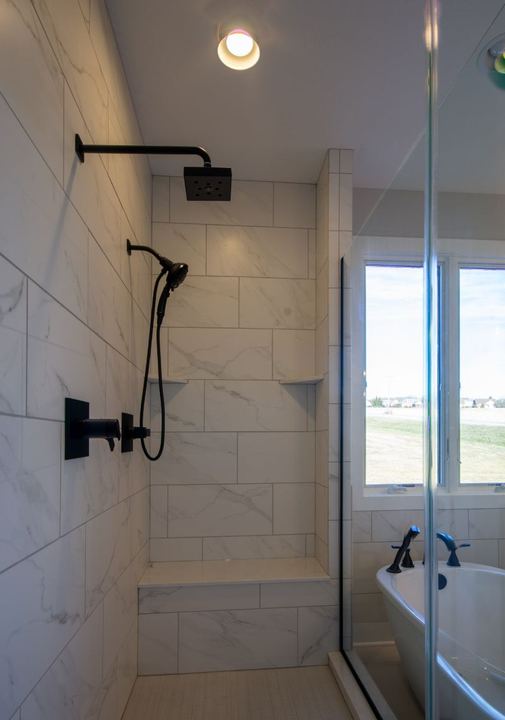 Walk-in shower with Calacatta marble-look tile, matte black fixtures, bench seat and freestanding tub beyond in Avon, IN