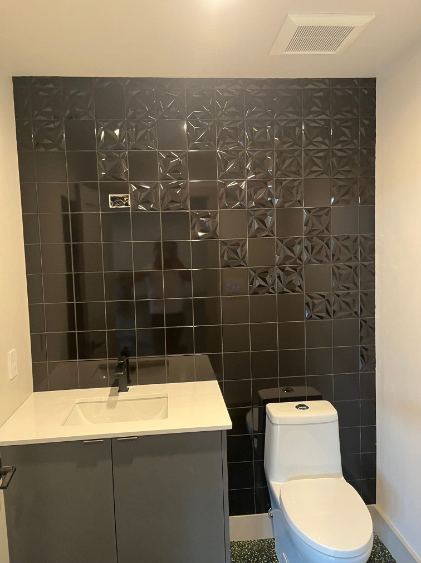 Powder room with glossy dimensional black tile accent wall, gray vanity and white countertop in Westfield, IN