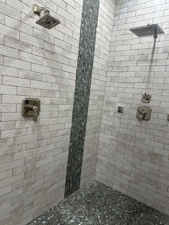 Dual-head walk-in shower with white brick-look tile walls, glass mosaic waterfall accent stripe and mosaic floor in Avon, IN