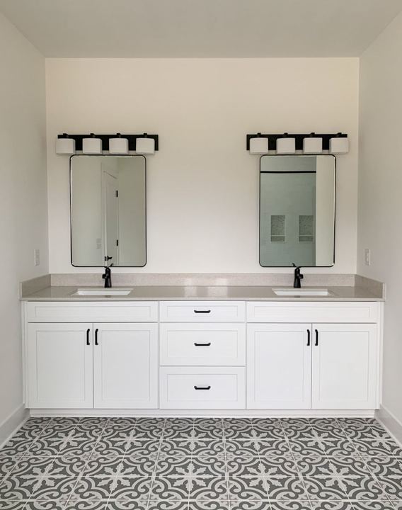 Master bathroom with gray and white encaustic patterned tile floor and white double vanity with black fixtures in Avon, IN