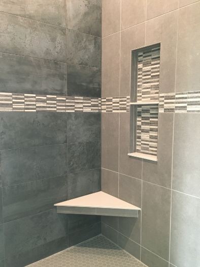 Gray tile master shower with linear glass mosaic accent band, matching niche trim and corner bench in Danville, IN