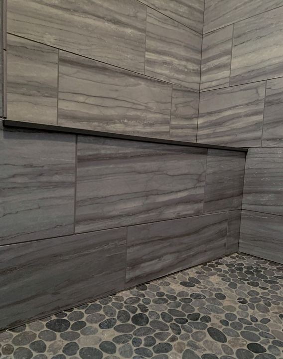 Shower with gray vein-cut stone-look tile walls, long niche and river pebble mosaic floor in Avon, IN