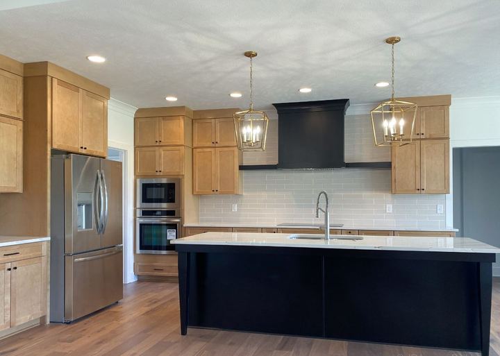 Maple kitchen with gray glass subway tile backsplash, black island and hickory hardwood floor in Avon, IN