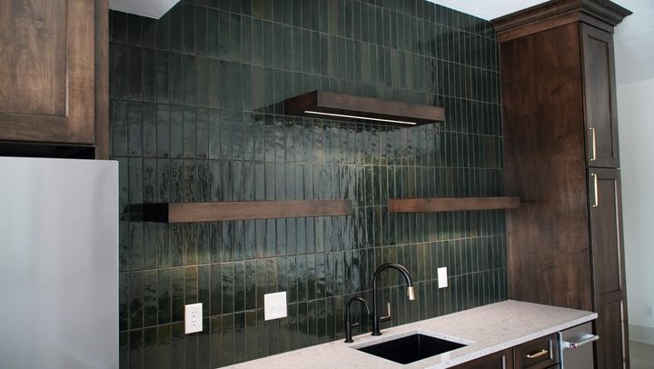 Vertically stacked glossy green tile backsplash wall with floating wood shelves and black faucet in Danville, IN