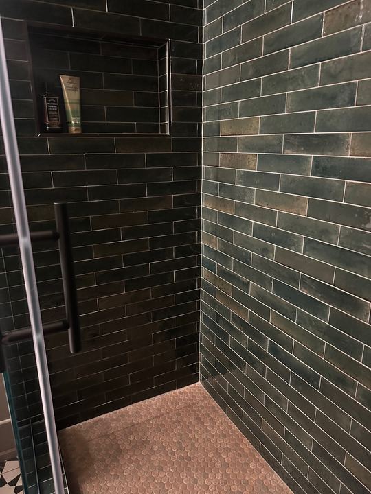 Walk-in shower with glossy dark green subway tile walls, tiled niche and copper penny round mosaic floor in Avon, IN