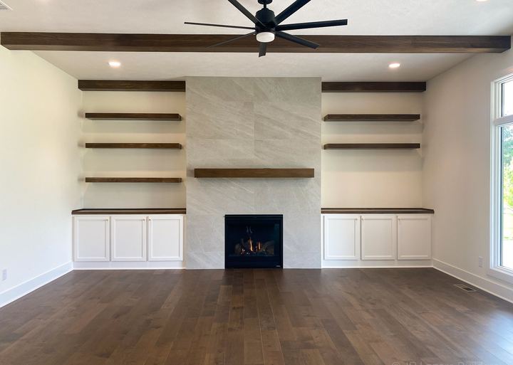 Great room with wide-plank dark hardwood floors, stone-look tile fireplace wall and floating shelves in Avon, IN