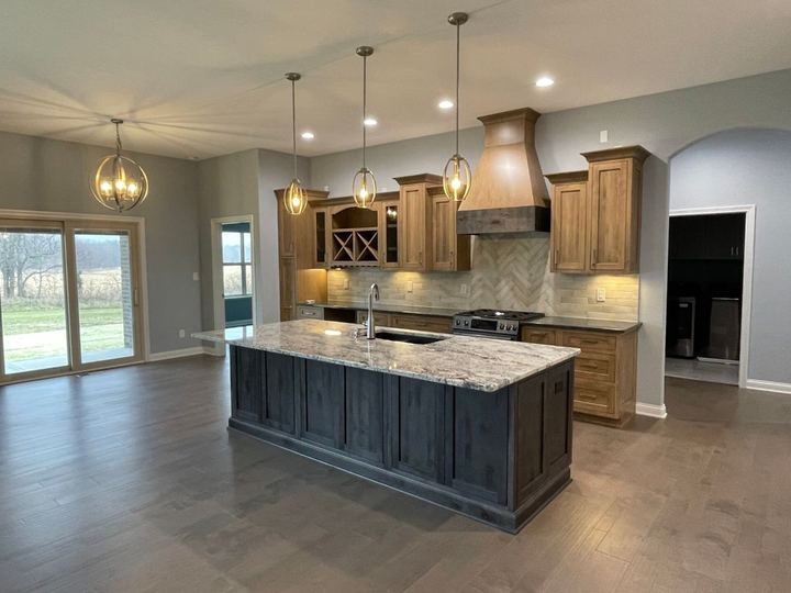 Kitchen with cream tile backsplash, herringbone accent above the range, granite-top island and hardwood floors in Plainfield, IN