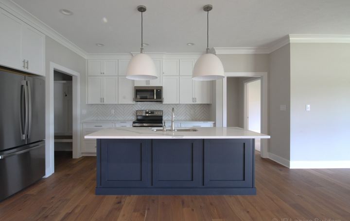 White kitchen with herringbone tile backsplash, navy blue island and hickory hardwood flooring in Avon, IN