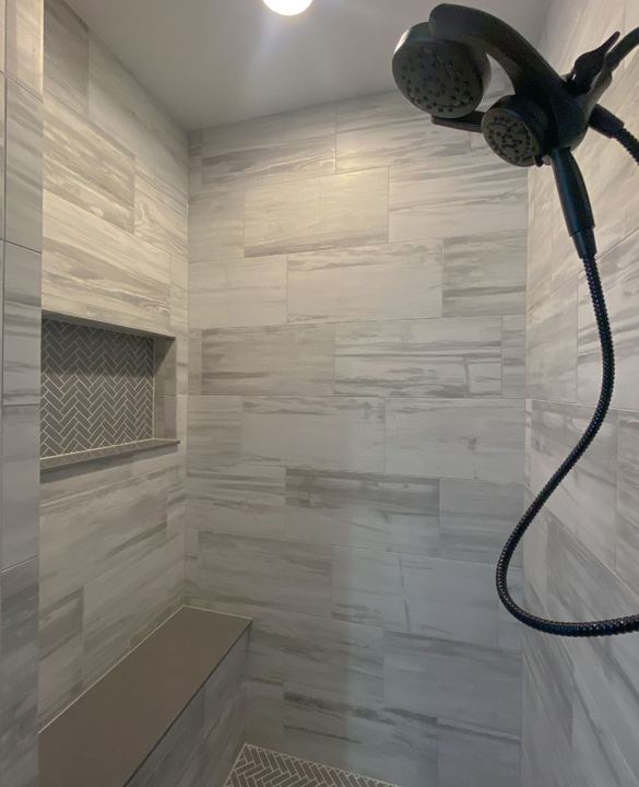 Walk-in shower with gray stone-look tile, herringbone mosaic niche and floor, bench and black dual shower head in Avon, IN