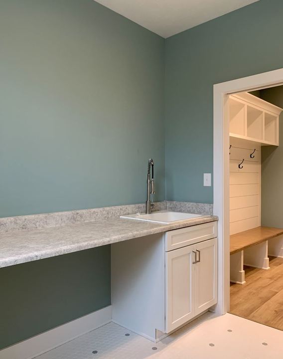Laundry room with white hex tile floor opening to a mudroom bench with plank flooring in Avon, IN