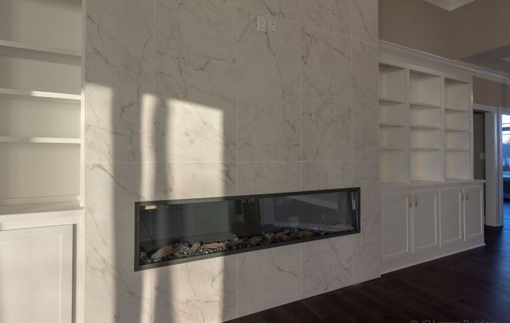 Floor-to-ceiling marble-look tile wall with linear fireplace and built-in bookcases in Avon, IN