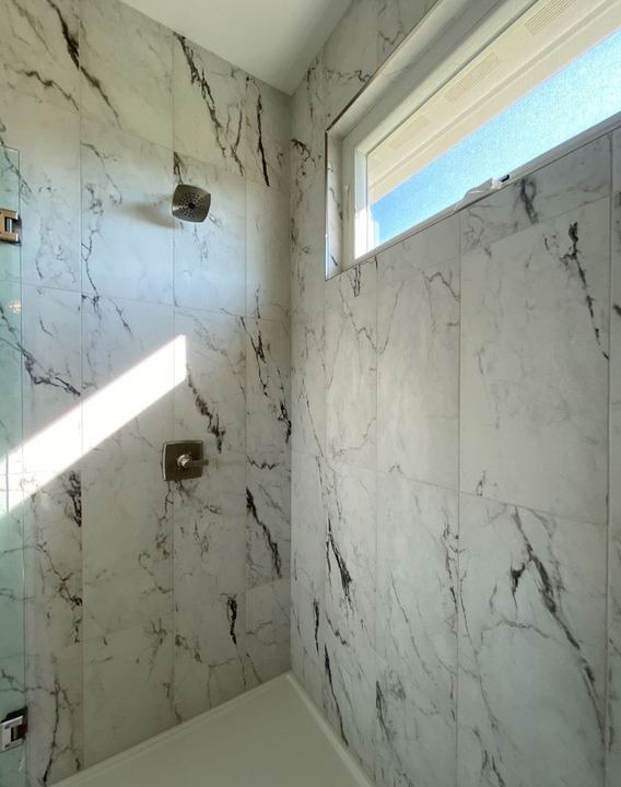 Walk-in shower with dramatic large-format marble-look tile walls and frosted transom window in Avon, IN