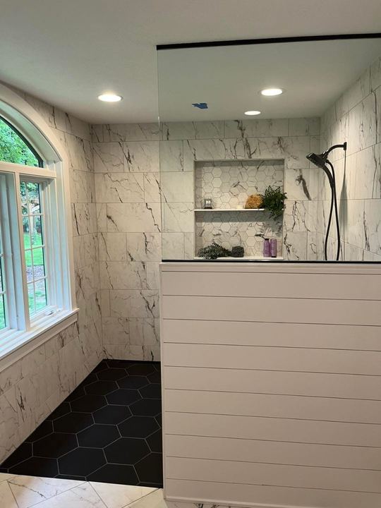 Custom walk-in shower with marble-look walls, black hexagon tile floor, hex mosaic niche and arched window in Pittsboro, IN