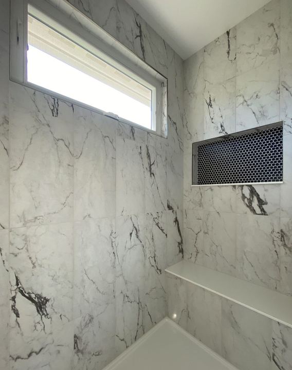 Shower with dramatic marble-look wall tile, black hex mosaic niche and quartz bench shelf in Avon, IN