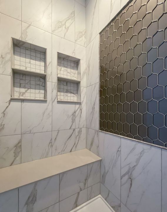 Marble-look tile shower with gray elongated hex accent wall, dual niches and quartz bench in Avon, IN