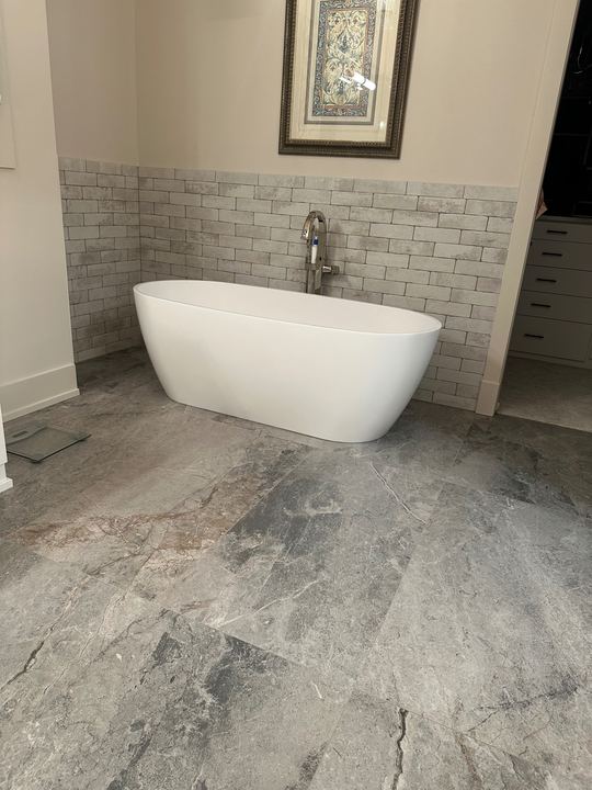 Freestanding soaker tub on gray marble-look tile floor with brick-look tile wainscot in Avon, IN