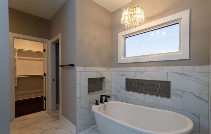 Freestanding tub against marble-look tile wainscot with hexagon mosaic niches and crystal chandelier in Avon, IN