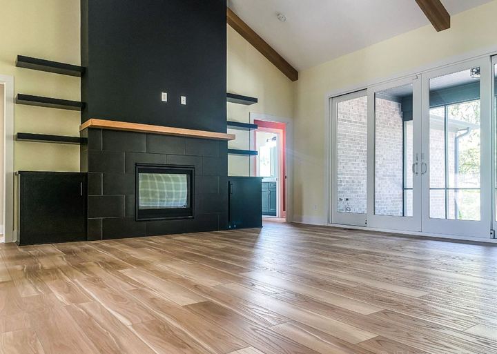 Living room with black tile fireplace, floating shelves and light wood-look plank flooring in Avon, IN