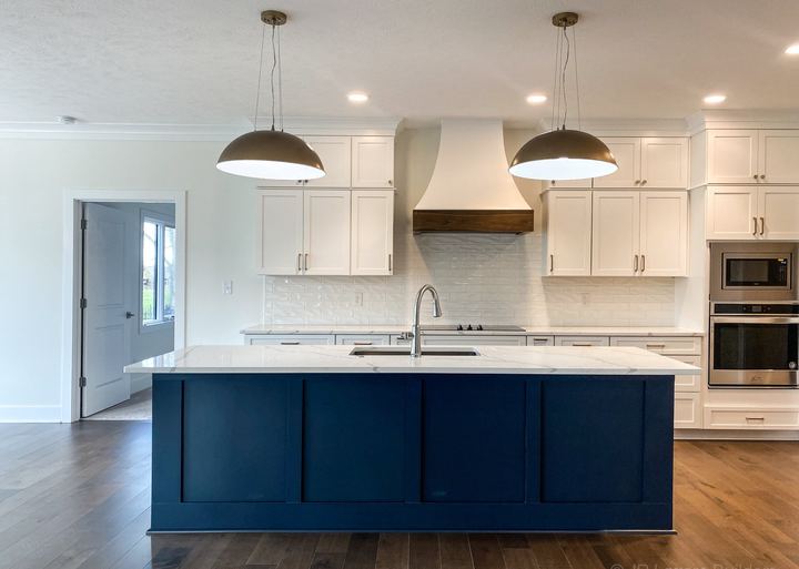 White kitchen with glossy subway backsplash, navy blue island, brass pendants and maple hardwood floors in Avon, IN
