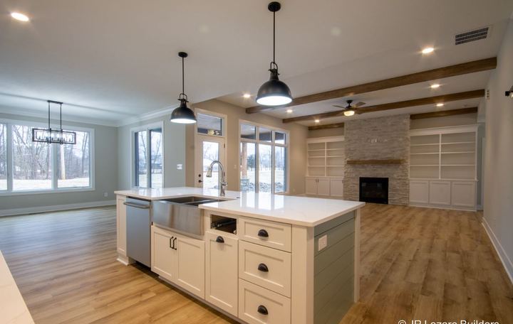 Open kitchen and living area with wood-look plank flooring, white island and stacked stone fireplace in Avon, IN