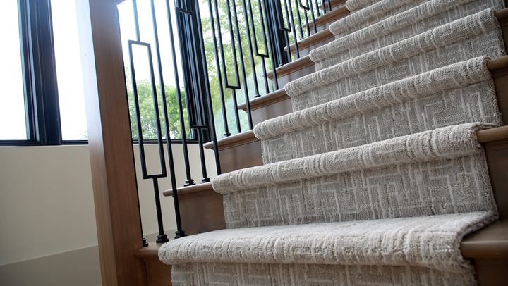 Staircase wrapped in textured gray patterned carpet with wood treads and iron balusters in Danville, IN