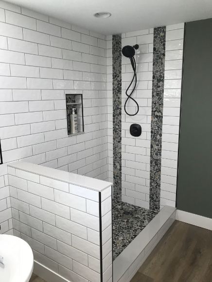 Walk-in shower with white subway tile, vertical pebble stone accent bands, matte black fixtures and tiled half wall in Greenwood, IN