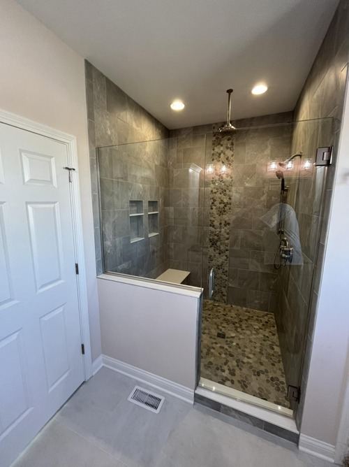Walk-in shower with gray stone-look tile, vertical pebble mosaic accent stripe and pebble floor behind glass in Danville, IN