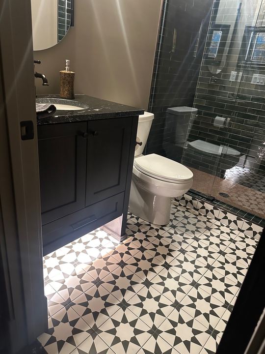 Bathroom with black and white star-pattern tile floor, dark green subway tile shower and black vanity in Avon, IN