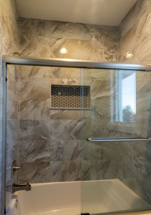 Tub and shower surround in large-format stone-look tile with hex mosaic niche and glass doors in Avon, IN