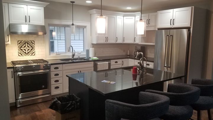 White kitchen with cream subway tile backsplash, decorative medallion inlay over the range and black granite island in Brownsburg, IN