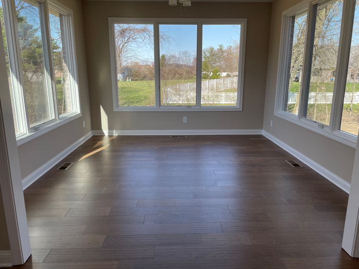 Sunlit sunroom with gray-brown wood-look plank flooring surrounded by picture windows in Plainfield, IN