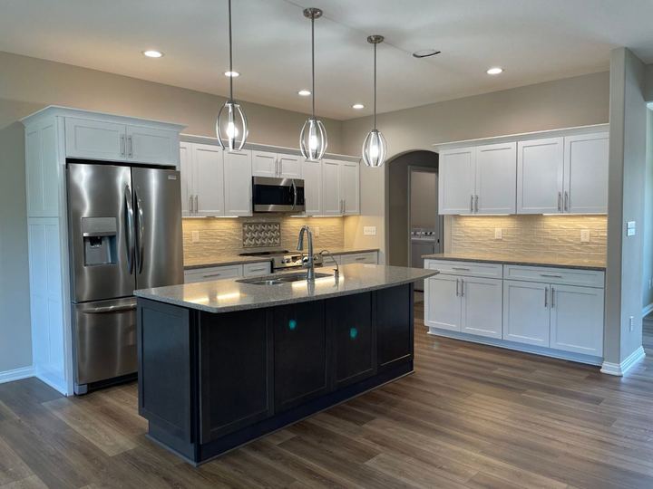 Kitchen with cream textured subway backsplash and accent insert, dark island and wood-look LVP flooring in Danville, IN