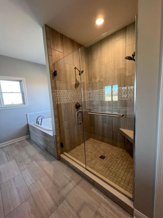 Walk-in shower with travertine-look tile, glass mosaic accent band, mosaic floor and frameless glass door in Brownsburg, IN