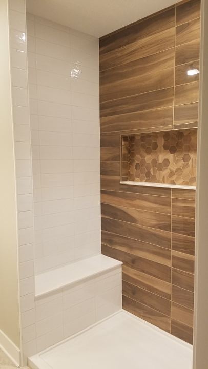 Walk-in shower with wood-look plank tile accent wall, hex mosaic niche, white subway walls and bench in Avon, IN