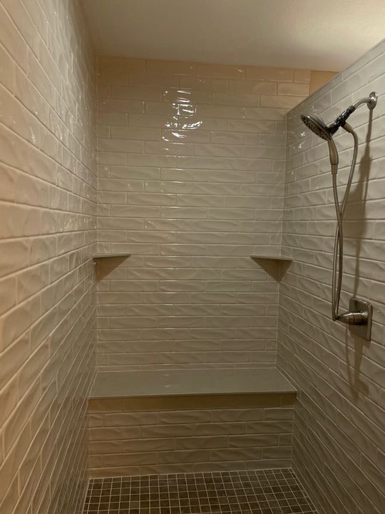 Walk-in shower with white wavy subway tile, built-in bench, corner shelves and mosaic floor in Avon, IN