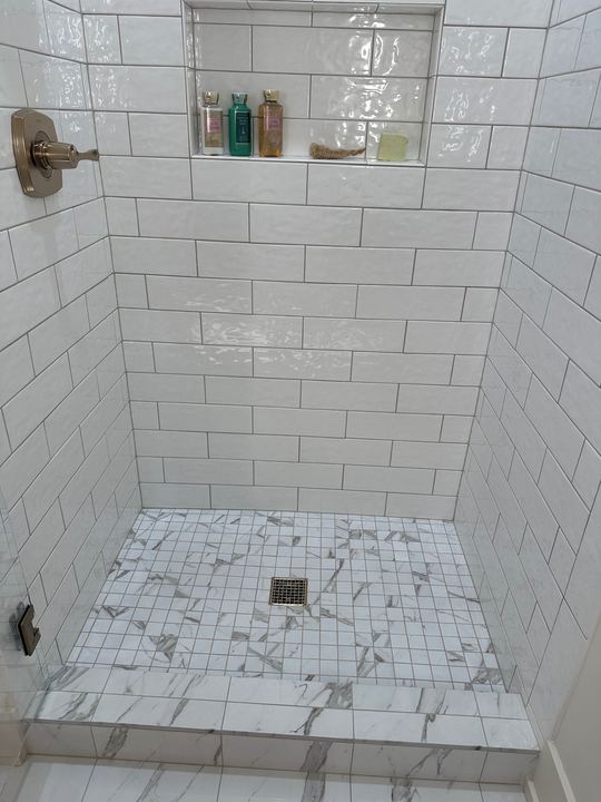 Walk-in shower with glossy white subway tile walls, marble-look mosaic floor and champagne bronze fixtures in Avon, IN
