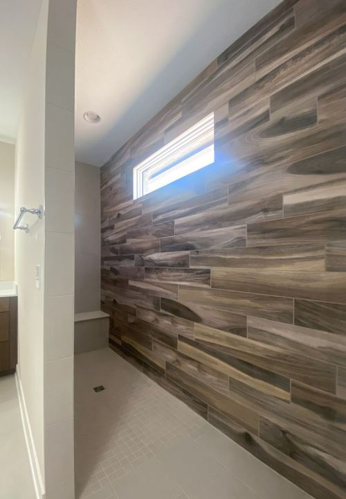 Walk-in master shower with wood-look plank tile accent wall, white mosaic floor and tiled bench in Avon, IN