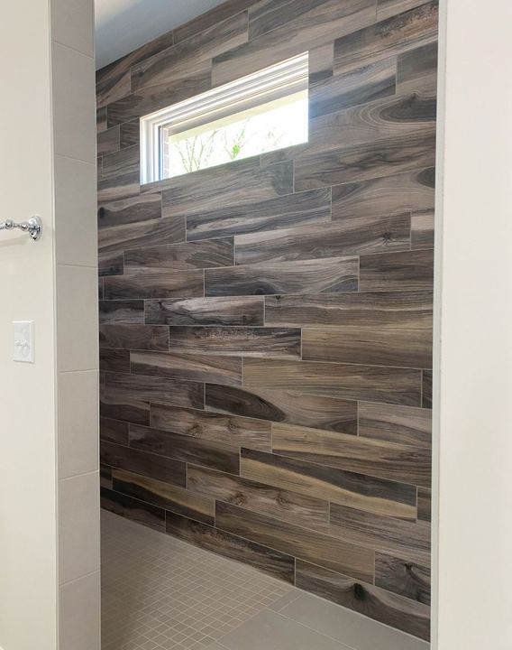 Walk-in shower with dramatic wood-look plank tile accent wall, transom window and gray mosaic floor in Avon, IN
