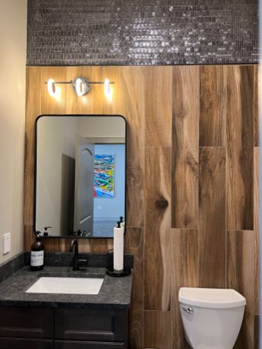Powder room with wood-look plank tile accent wall, glossy mosaic band above and black granite vanity top in Westfield, IN