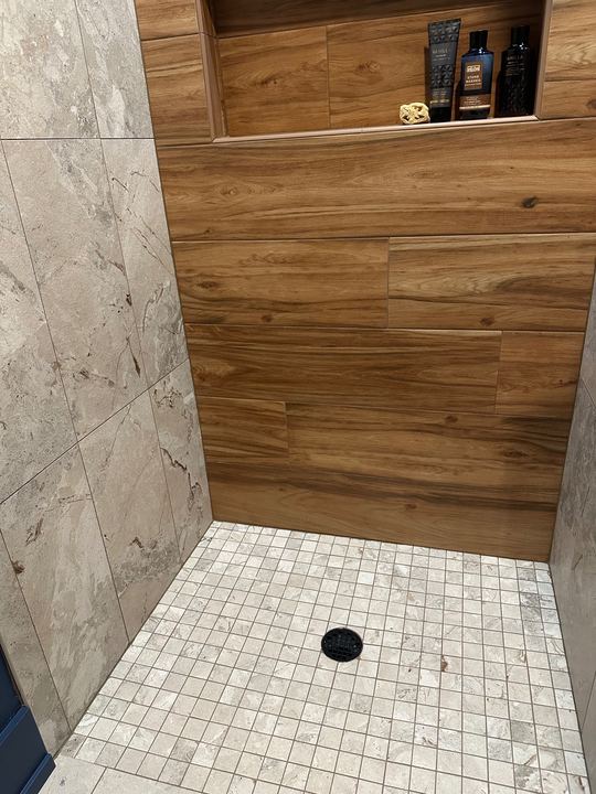 Tile shower pairing wood-look plank accent wall with marble-look walls, mosaic floor and wide shampoo niche in Avon, IN